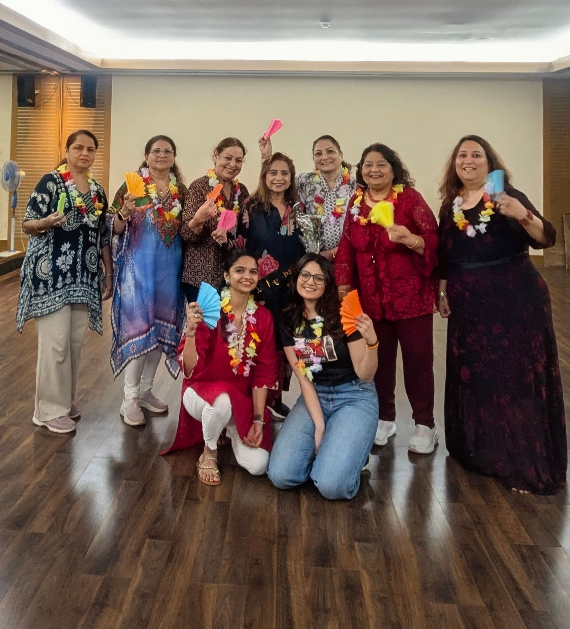 Members of the Andheri West club standing together in the Yoga Room wearing flower garlands and holding paper fans, at a themed session.