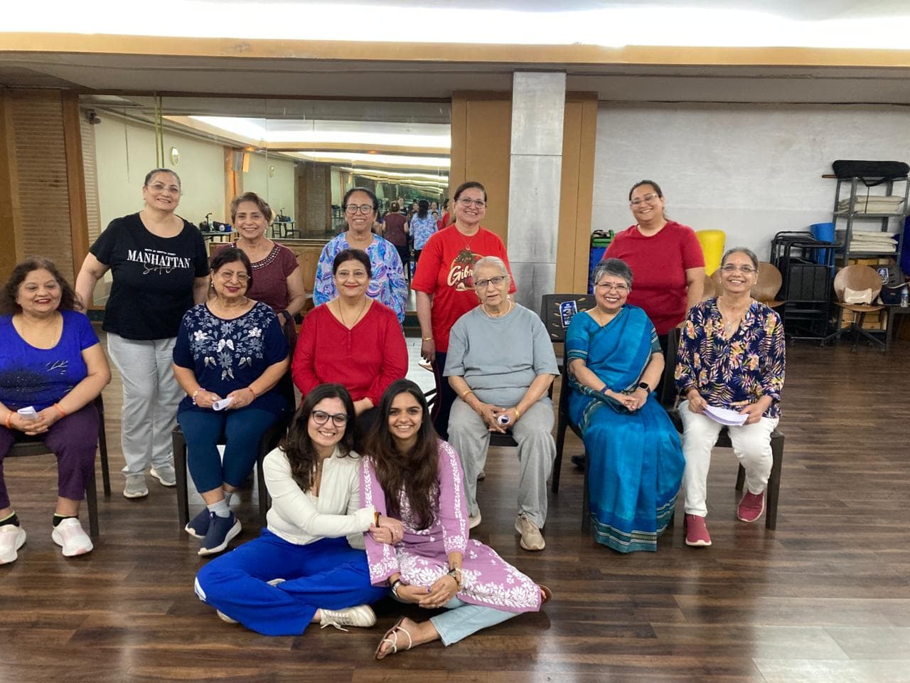 Members of the Andheri West club in the Yoga Room at The Classique Club, some seated on chairs and some standing behind, smiling at the camera after a session.